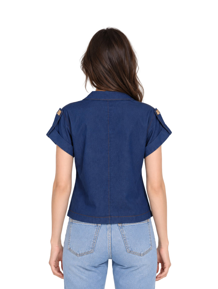 Mujer vistiendo blusa de mezclilla azul con botones frontales y pantalones de mezclilla claros.