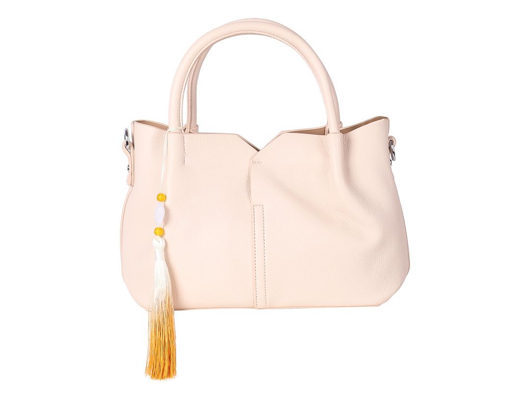 Bolso de mano color beige con asas redondeadas y un adorno de borla en tonos blanco y amarillo.