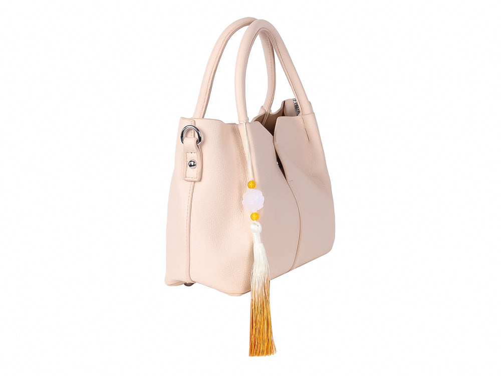 Bolso de mano color beige con asas redondeadas y un adorno de borla en tonos blanco y amarillo.