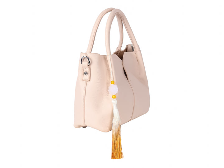 Bolso de mano color beige con asas redondeadas y un adorno de borla en tonos blanco y amarillo.