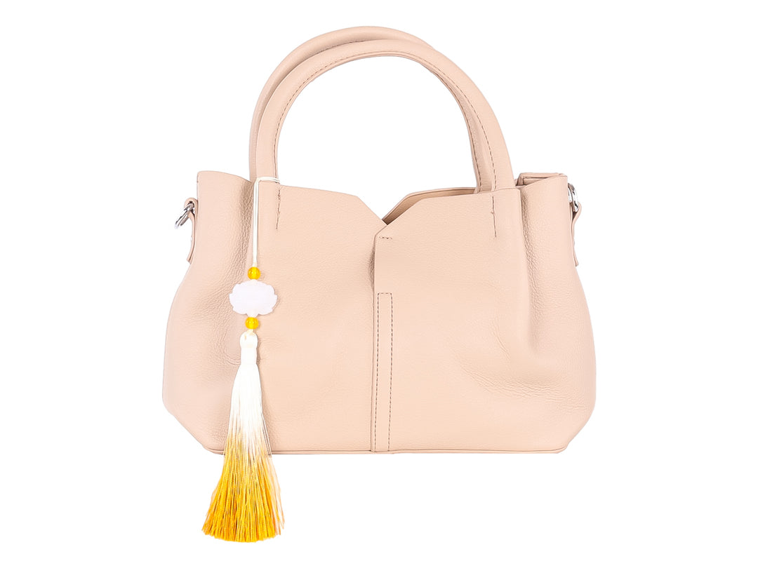 Bolso de hombro color taupe con asa superior y un adorno de borla en colores blanco y amarillo.