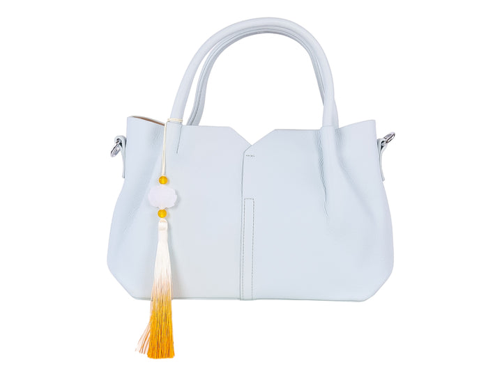 Bolso de hombro color azul claro con asa superior y un accesorio colgante de borla amarilla y blanca.