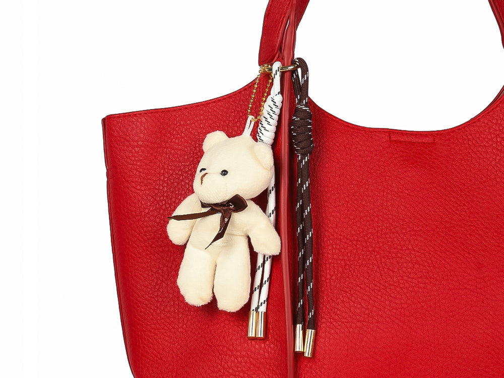 Bolsa de hombro color rojo con textura rugosa y un pequeño oso de peluche blanco como accesorio colgante.