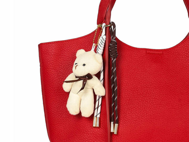 Bolsa de hombro color rojo con textura rugosa y un pequeño oso de peluche blanco como accesorio colgante.