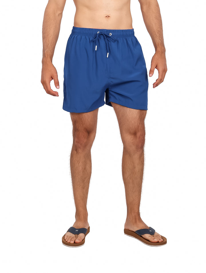 Hombre vistiendo un traje de baño corto color azul marino con cordones blancos.
