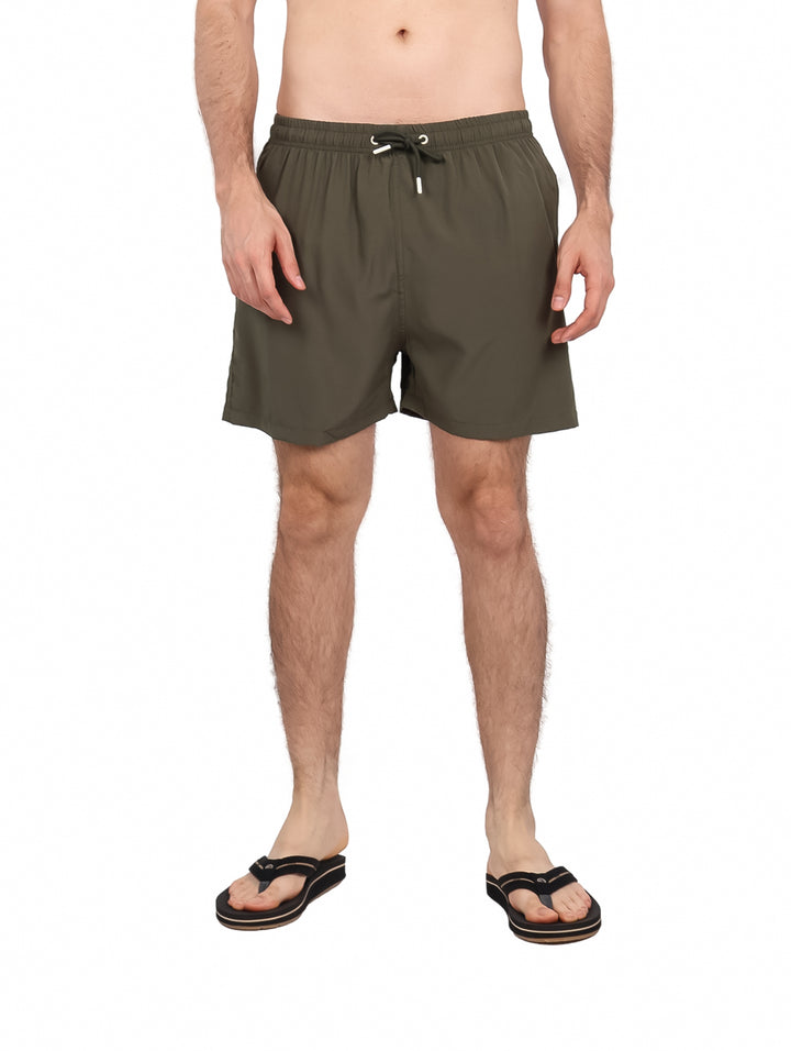 Hombre vistiendo un traje de baño corto color olivo con cordón blanco y sandalias negras.