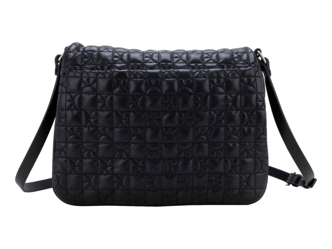 Bolso de hombro color negro con textura acolchada geométrica, correa ajustable y detalle circular central.