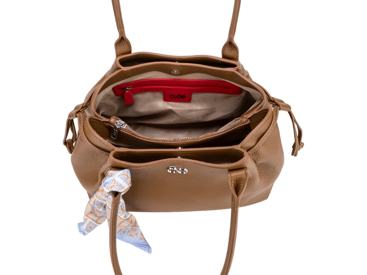 Bolsa de hombro Cloe color camel en cuero granulado con un pañuelo azul y blanco amarrado al asa.