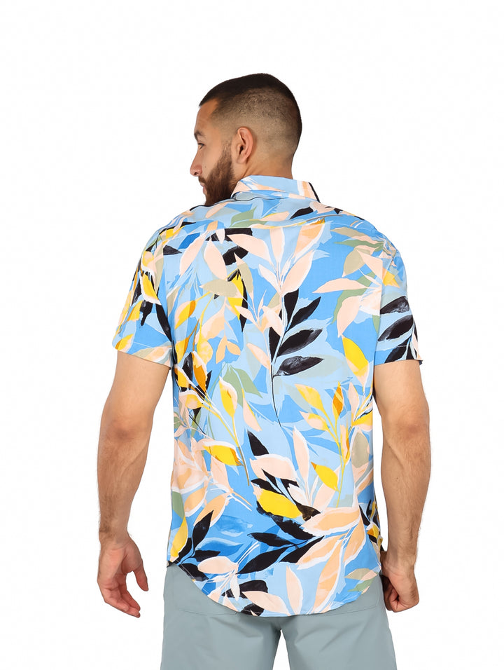 Hombre vistiendo camisa de manga corta con estampado floral multicolor en tonos azul, amarillo y blanco.