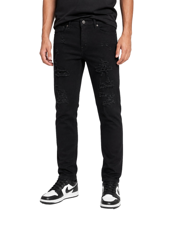 Hombre vistiendo jeans negros con roturas y tenis blancos y negros sobre fondo blanco.