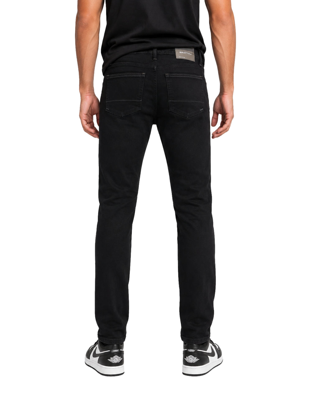 Hombre vistiendo jeans negros con roturas y tenis blancos y negros sobre fondo blanco.
