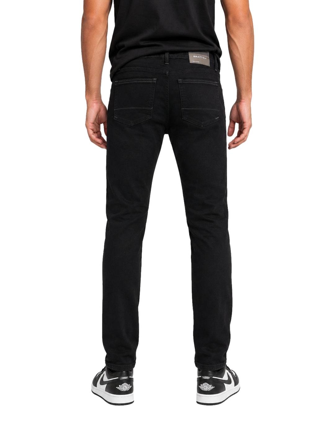 Hombre vistiendo jeans negros con roturas y tenis blancos y negros sobre fondo blanco.