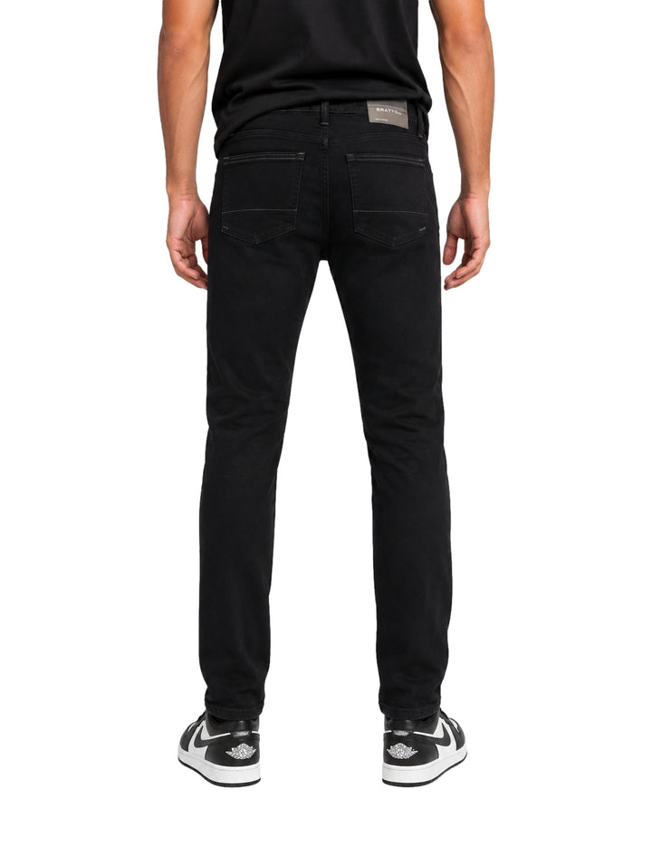 Hombre vistiendo jeans negros con roturas y tenis blancos y negros sobre fondo blanco.