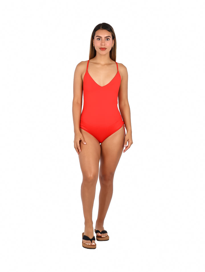 Mujer vistiendo un traje de baño enterizo color rojo fuego con cuello en V y tirantes delgados.