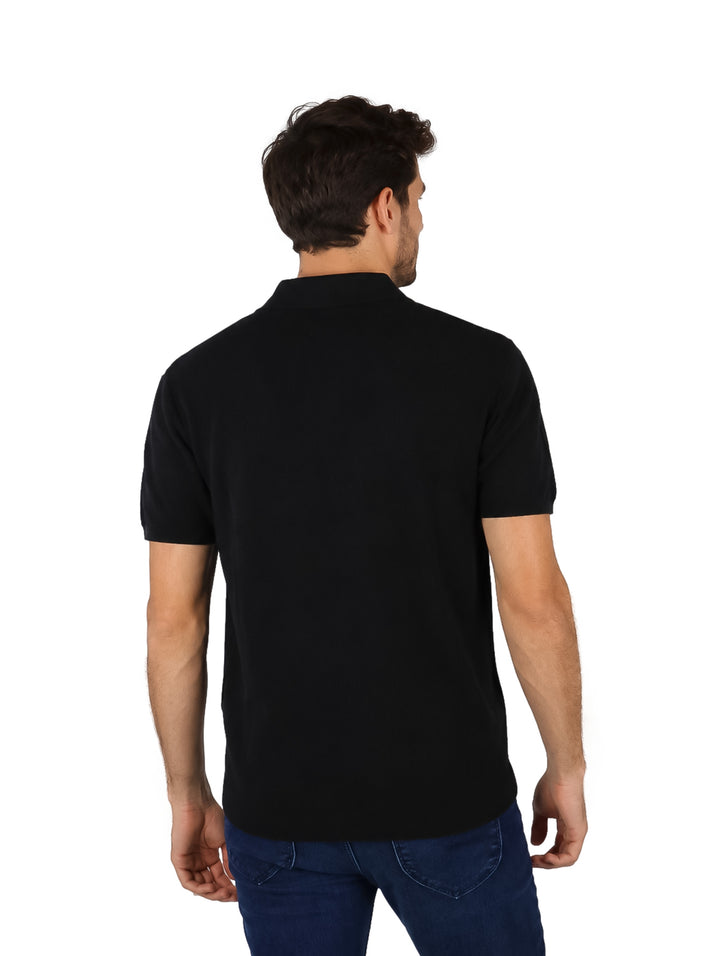 Hombre vistiendo una playera polo de color negro y pantalones azules.