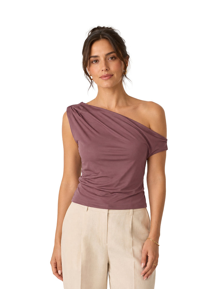 Mujer vistiendo una blusa morada asimétrica de un solo hombro y pantalones beige.