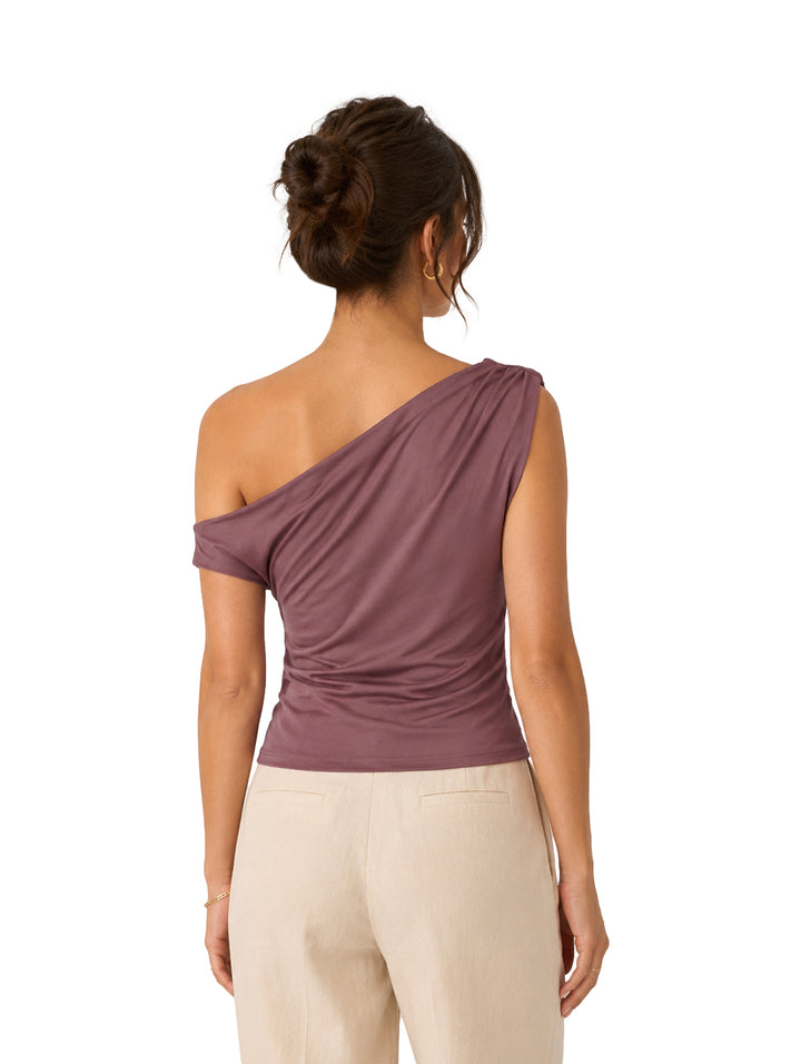 Mujer vistiendo una blusa morada asimétrica de un solo hombro y pantalones beige.