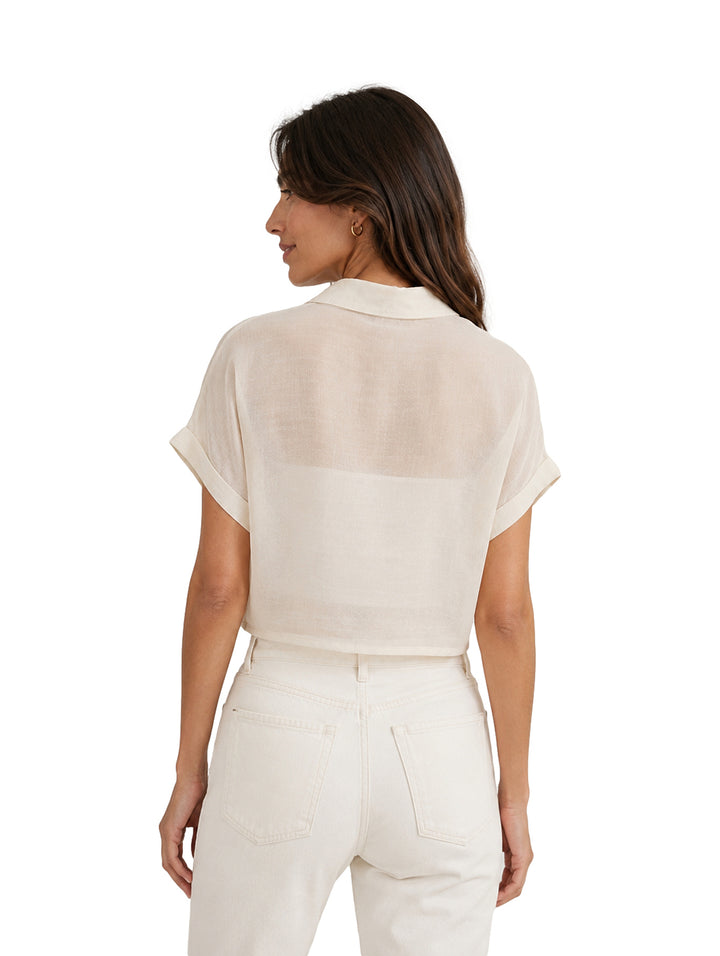 Mujer vistiendo blusa corta color blanco con cierre anudado al frente y pantalones blancos.