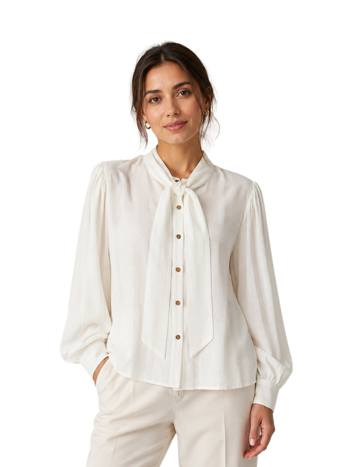 Mujer vistiendo una camisa blanca de manga larga con cuello de lazo y botones frontales.