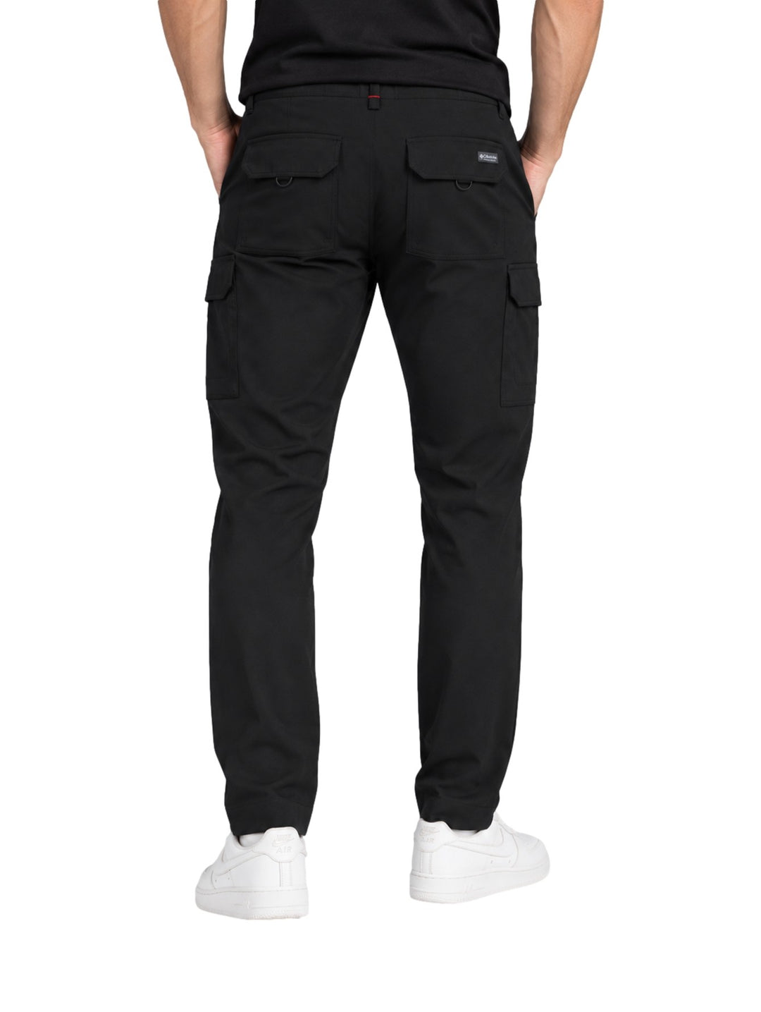 Hombre vistiendo pantalones cargo Columbia Trail color negro con bolsillos laterales y calzado blanco.