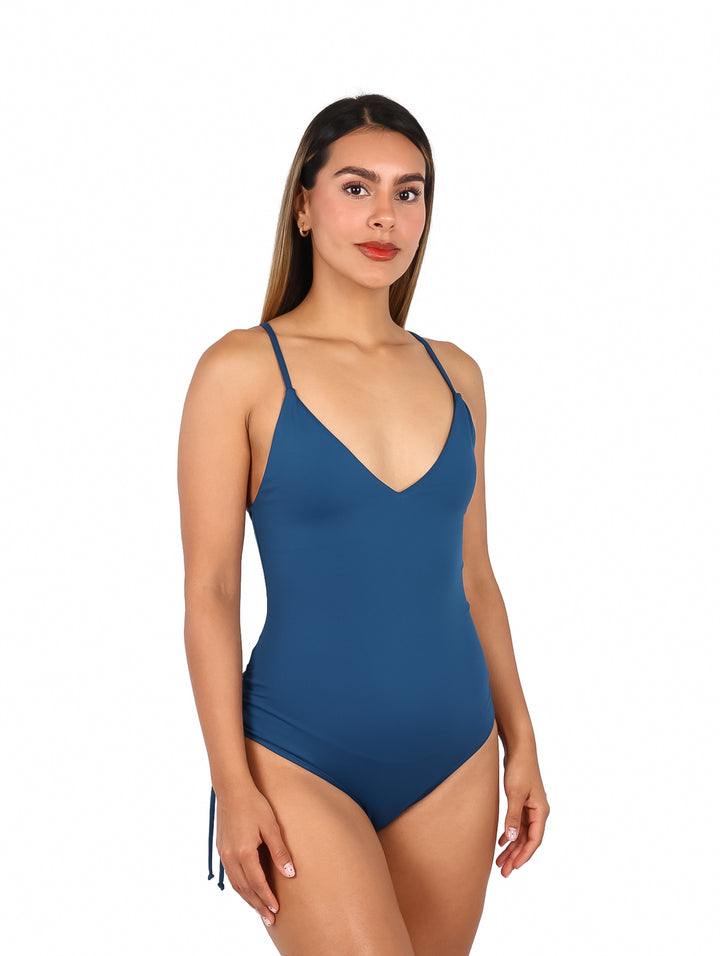 Mujer vistiendo un traje de baño enterizo color azul denim con cuello en V y tirantes delgados.