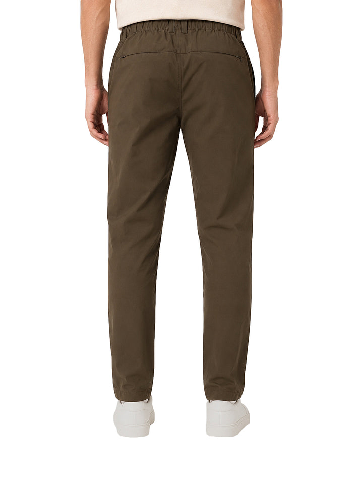 Hombre vistiendo pantalón color olivo oscuro de corte casual y tenis blancos.