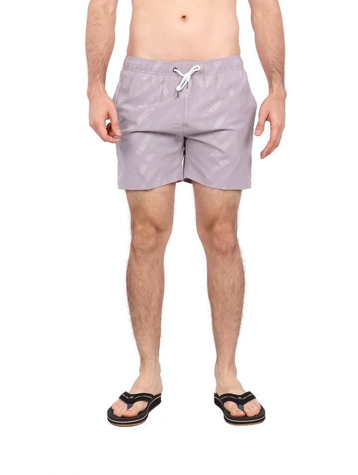 Hombre vistiendo traje de baño corto color gris claro con patrón geométrico y cordón blanco.