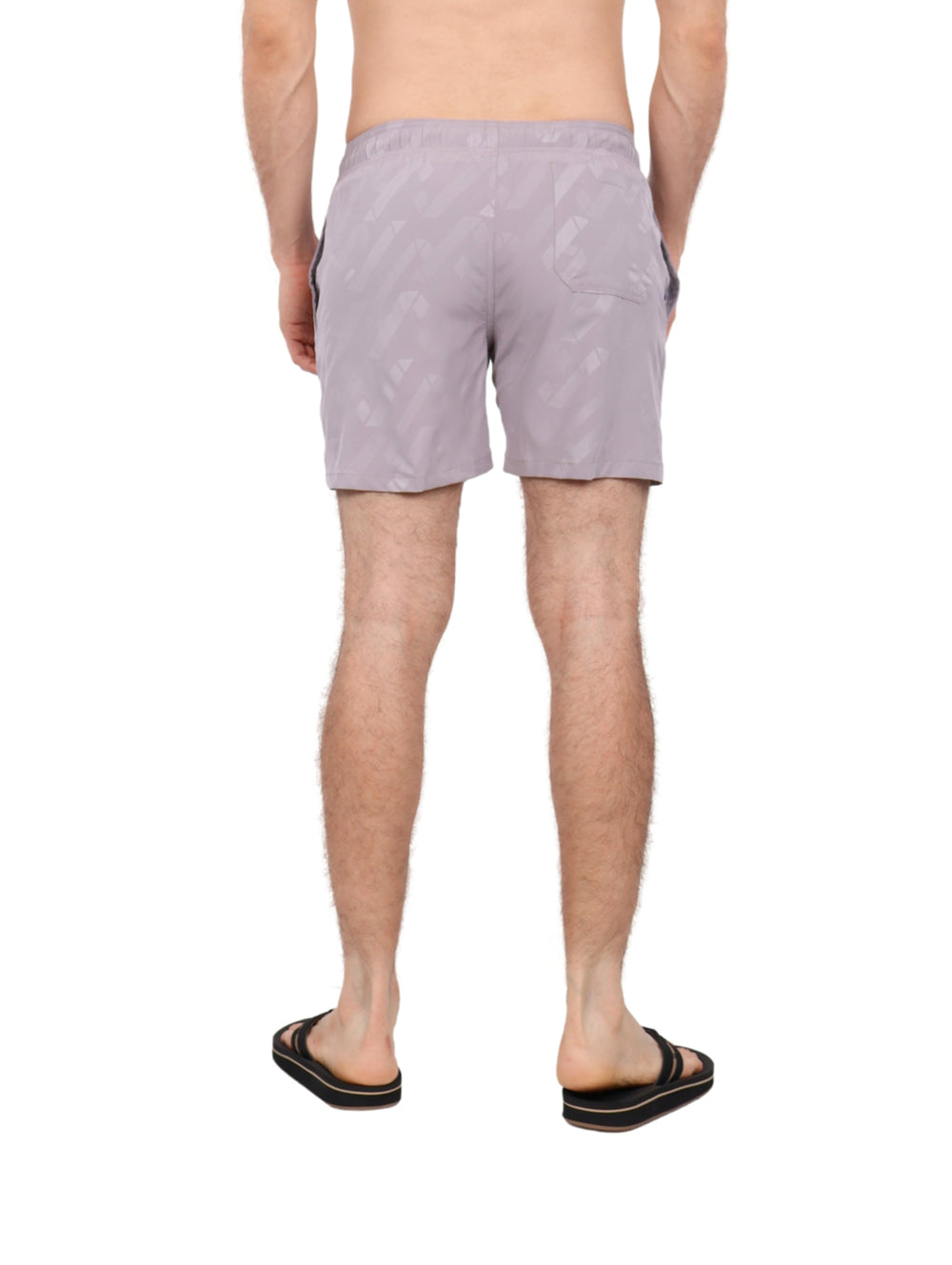 Hombre vistiendo traje de baño corto color gris claro con patrón geométrico y cordón blanco.
