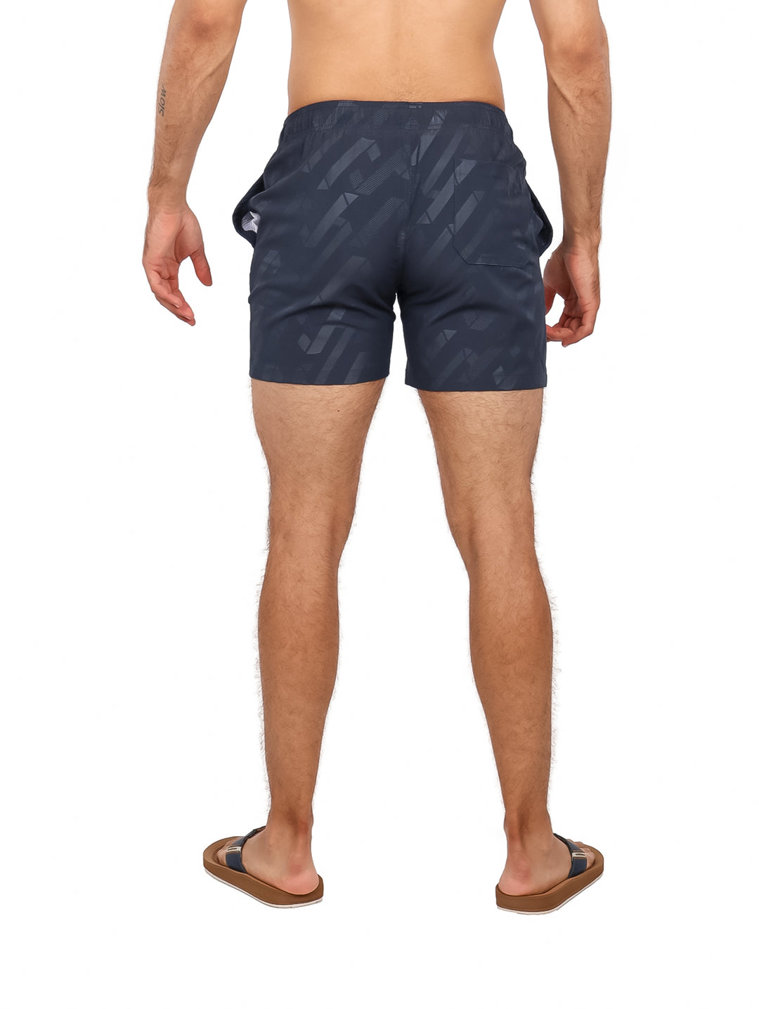 Hombre vistiendo traje de baño corto color azul marino con estampado geométrico y cordón blanco.