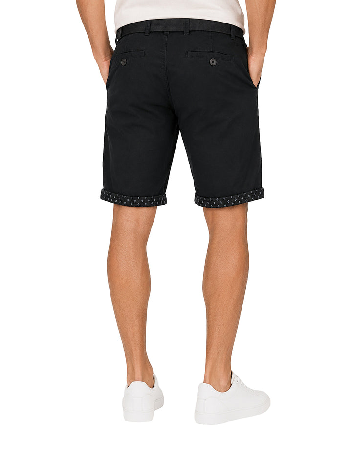 Hombre vistiendo bermuda color negro con cinto a juego y tenis blancos.