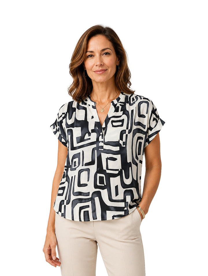 Mujer vistiendo blusa blanca con estampado geométrico negro, cuello en V y manga corta.