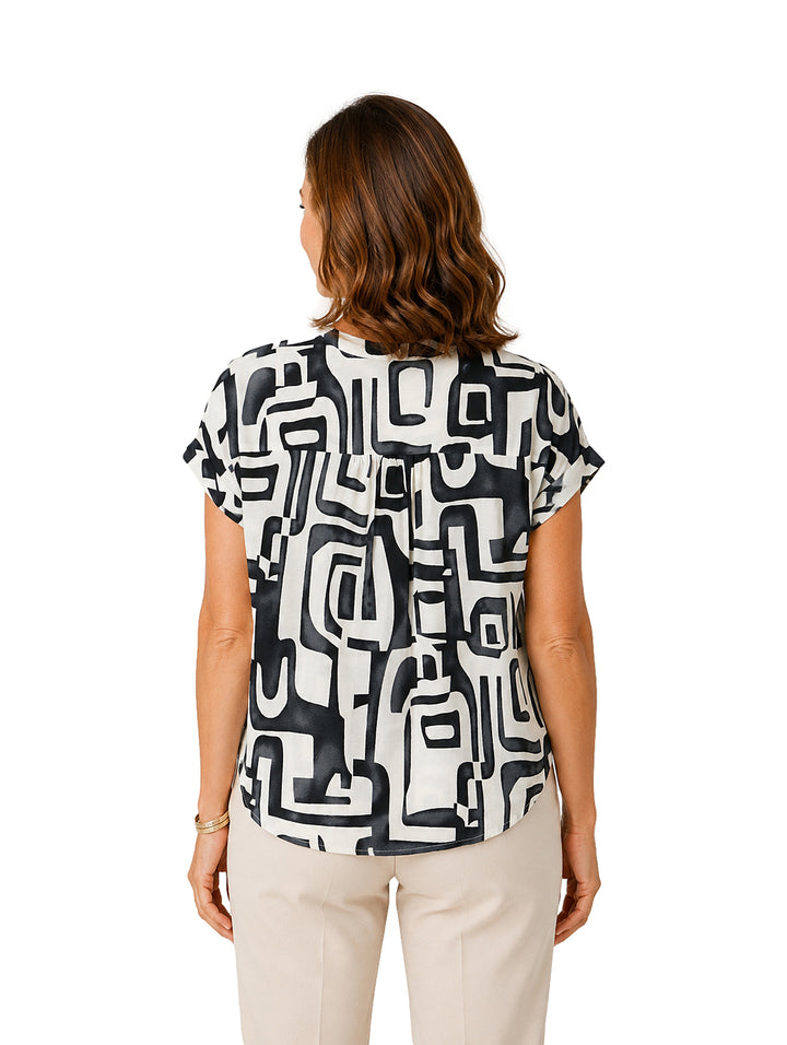 Mujer vistiendo blusa blanca con estampado geométrico negro, cuello en V y manga corta.