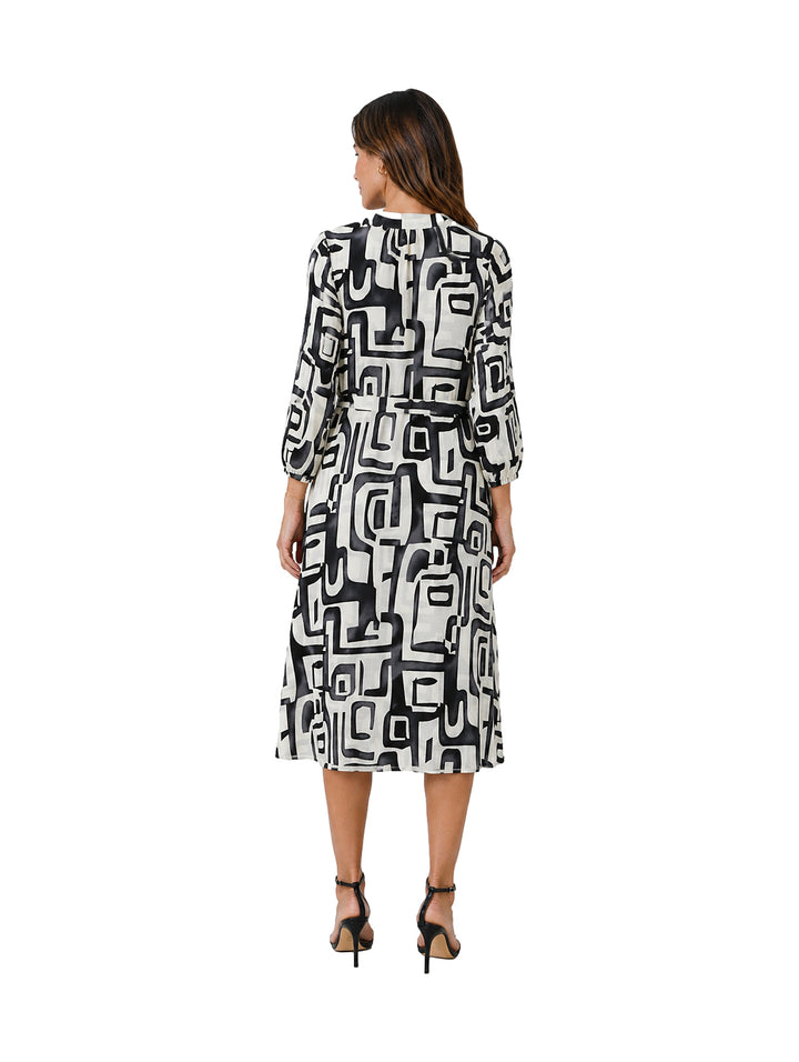 Mujer vistiendo un vestido midi de manga larga con estampado geométrico en blanco y negro.