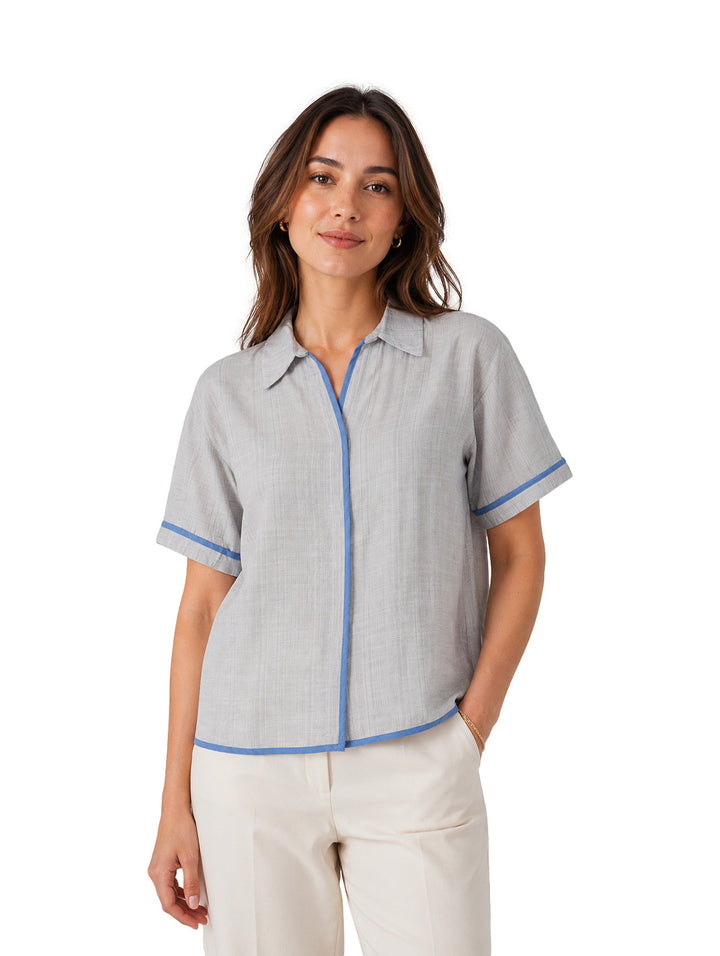 Mujer vistiendo una camisa gris de manga corta con ribetes azules en el cuello, botones y mangas.