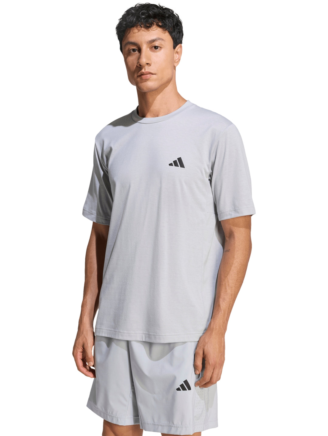 Hombre vistiendo conjunto deportivo Adidas de color gris compuesto por camiseta y shorts.