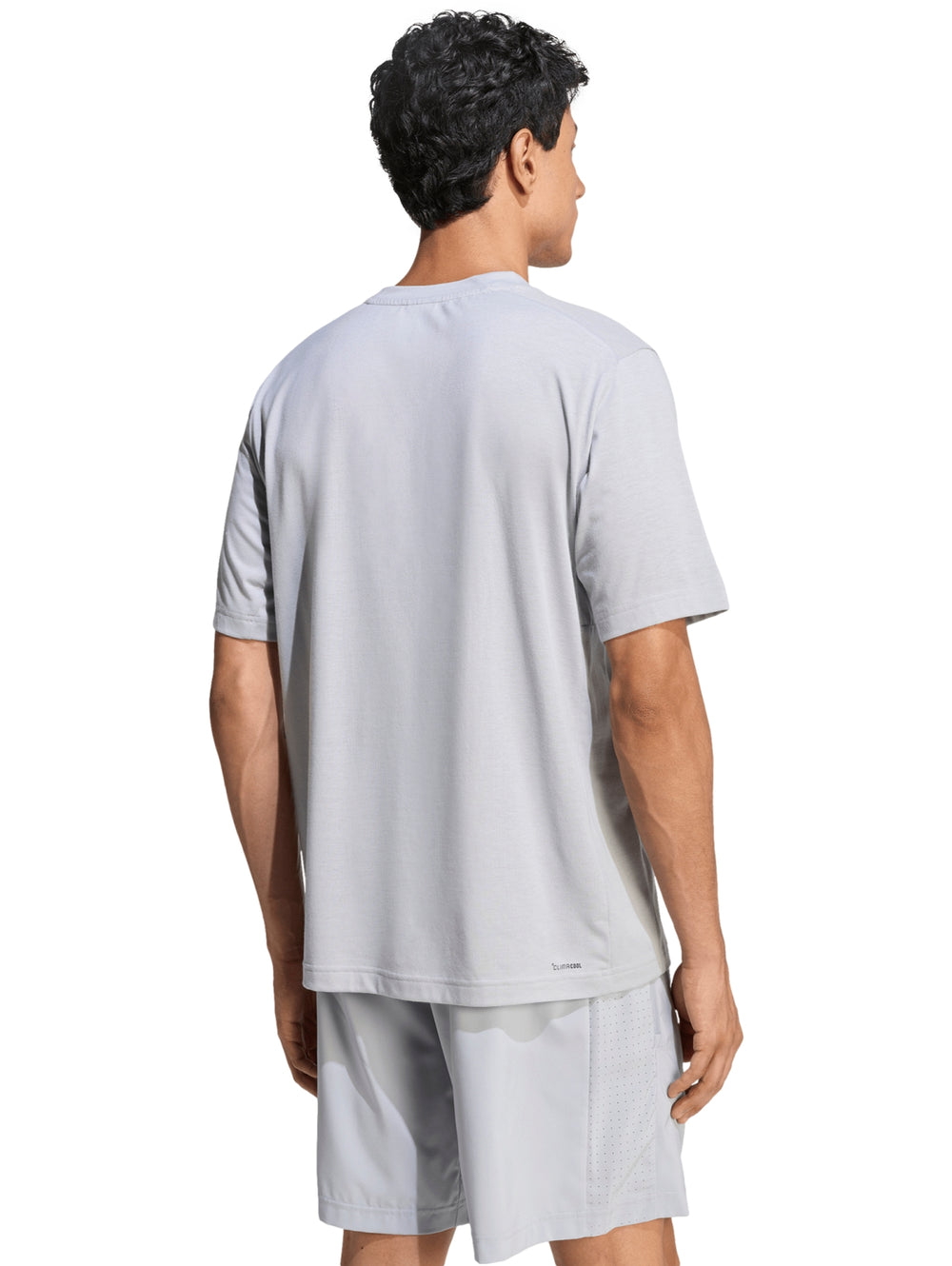 Hombre vistiendo conjunto deportivo Adidas de color gris compuesto por camiseta y shorts.