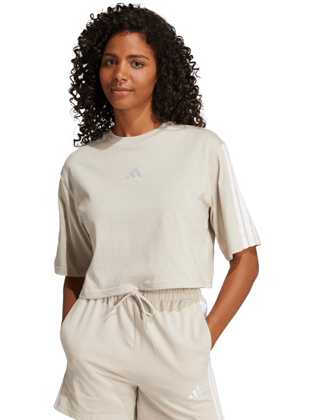 Mujer vistiendo playera crop top y shorts deportivos color beige con rayas blancas de Adidas.