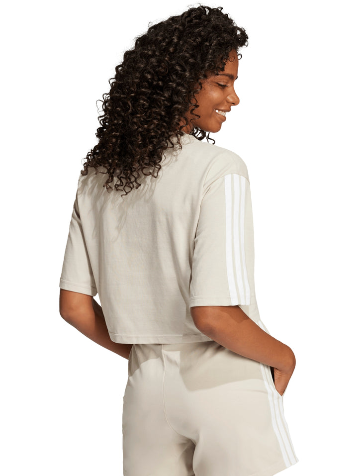 Mujer vistiendo playera crop top y shorts deportivos color beige con rayas blancas de Adidas.