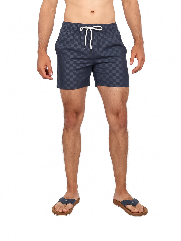 Hombre vistiendo traje de baño corto color navy con patrón de cuadros y cordón blanco.