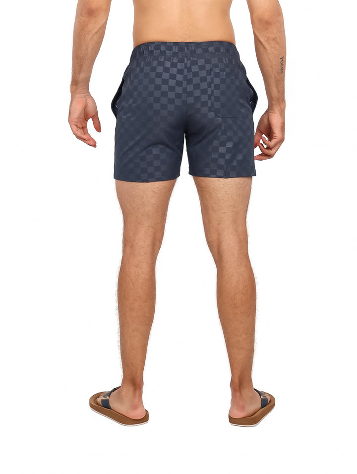 Hombre vistiendo traje de baño corto color navy con patrón de cuadros y cordón blanco.