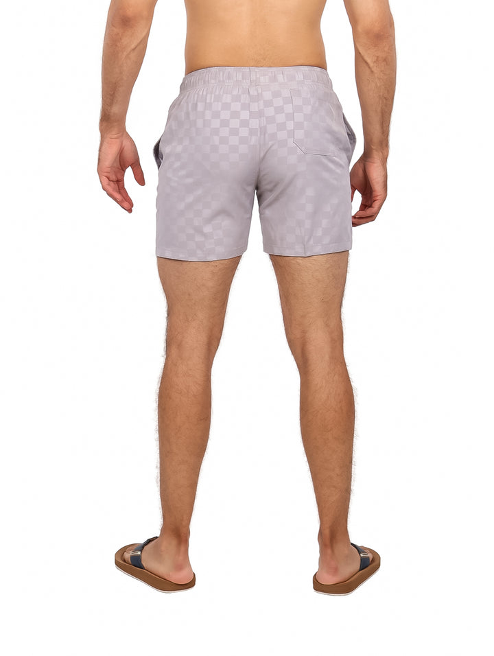 Hombre vistiendo traje de baño corto color gris claro con patrón de cuadros y cordón blanco.