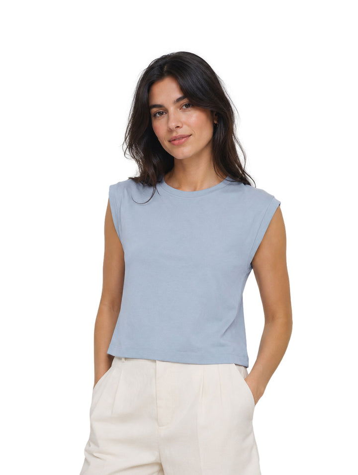 Mujer modelando una blusa azul sin mangas de cuello redondo y pantalones color crema.