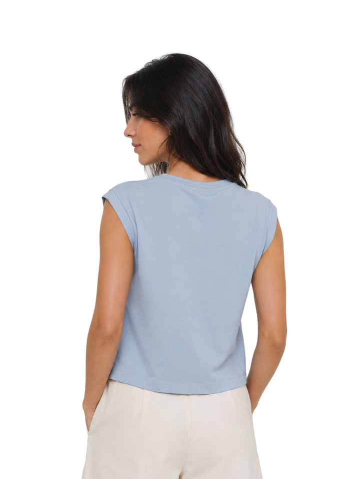 Mujer modelando una blusa azul sin mangas de cuello redondo y pantalones color crema.