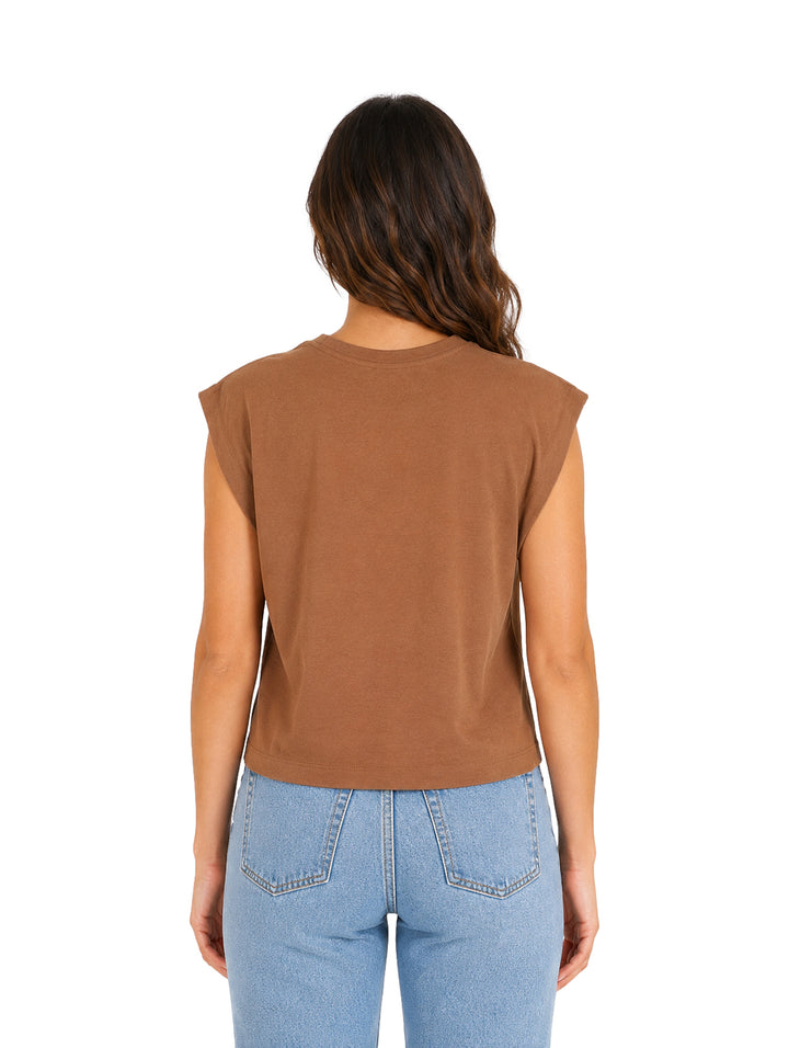 Mujer vistiendo una blusa marrón sin mangas y jeans azules sobre fondo blanco.