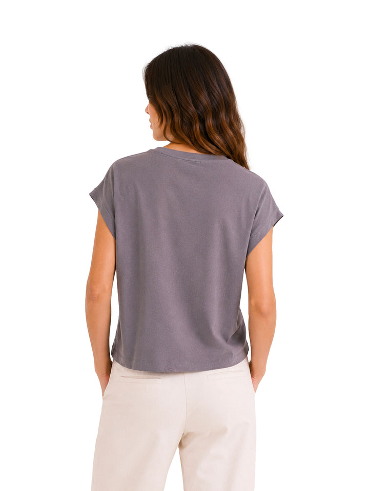 Mujer vistiendo una blusa color gris de manga corta y pantalones color crema.