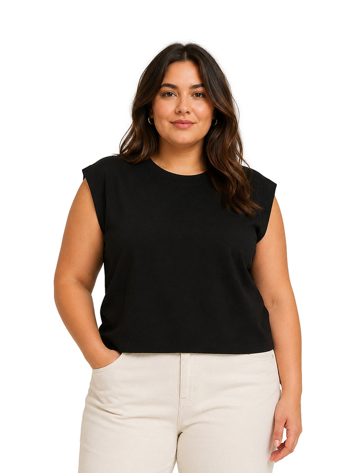 Mujer vistiendo una blusa negra sin mangas de cuello redondo y pantalones color crema.