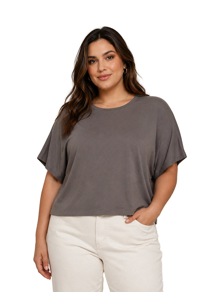 Mujer vistiendo blusa holgada color gris y pantalones blancos.