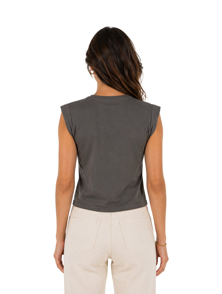Mujer vistiendo una blusa sin mangas color gris oscuro y pantalones color blanco roto.
