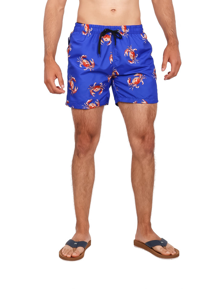 Hombre vistiendo traje de baño corto color azul con estampado de cangrejos rojos.