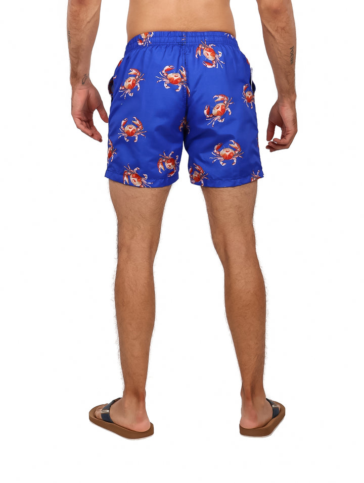 Hombre vistiendo traje de baño corto color azul con estampado de cangrejos rojos.